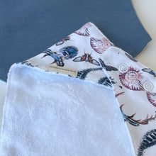 Load image into Gallery viewer, close up of white patterned gender neutral bib with blue bib in background