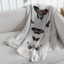 Load image into Gallery viewer, white organic cotton baby quilt with butterfly print draped on a sofa
